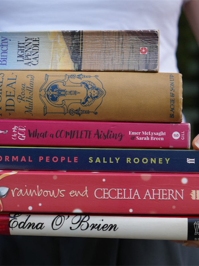 Photograph of a person holding a stack of romance novels.